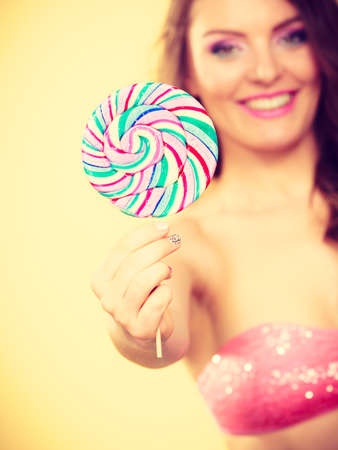 Woman attractive cheerful girl holding big lollipop candy in hand. Sweet food and enjoying concept. Studio shot bright yellow backgroundの写真素材