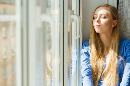 Happy woman with long blonde hair sitting on windowsill and relaxing, meditate or thinking.の写真素材