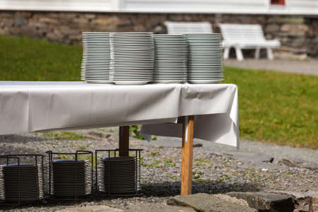 Big piles of fresh clean plates drying outside on table with white tableclothの写真素材