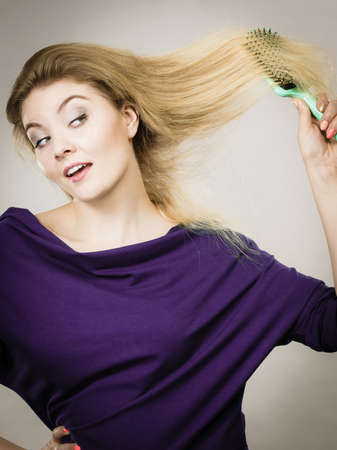 Happy woman combing her hair with brush. Young smiling female with natural blond straight long hairs, studio shot on greyの写真素材