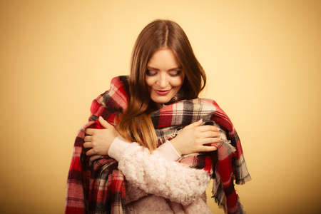 Autumnal outfit concept. Young long haired woman wearing warm autumn clothing woolen checked scarf on beige, studio shotの写真素材