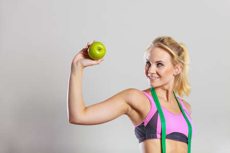 Time for diet slimming weight loss. Health care and healthy nutrition. Young fitness woman fit girl with measure tape and apple fruit on grayの写真素材