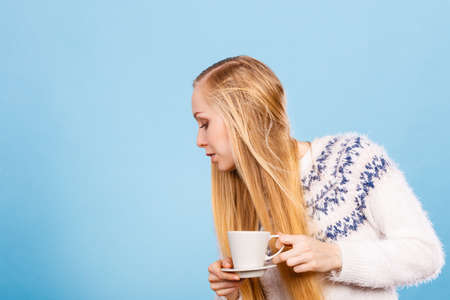 Morning drinks, enjoying morning free time concept. Blonde woman drinking hot coffee or tea from white cup to feel warmの写真素材