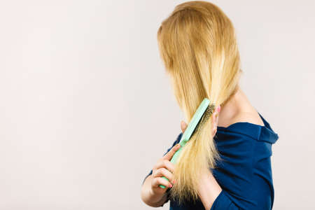 Woman combing her hair with brush. Young female with beautiful natural blond straight long hairs, studio shot on greyの写真素材