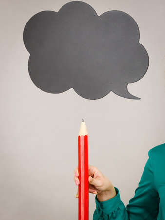 Woman holding pencil, black thinking or speech bubble next to her, grey backgroundの写真素材