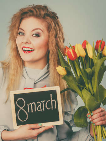 International women day. Beautiful woman blonde hair fashion make up holding red yellow tulips and frame board with message 8 march. Toned imageの写真素材