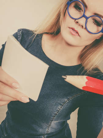 Serious student girl or female teacher, business coach holding huge red pencil and note paper,...