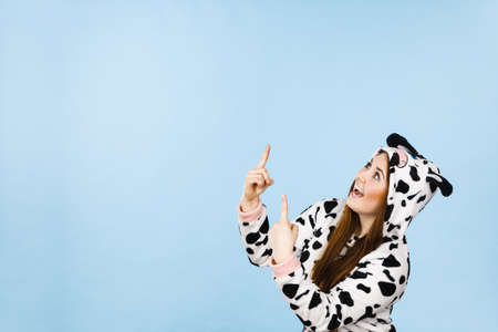 Happy teenage girl in funny nightclothes, pajamas cartoon style pointing up with positive surprised face expression, studio shot on blue. Advertisement conceptの写真素材