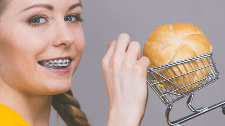 Buying gluten food products concept. Happy woman holding shopping cart trolley with bun breal roll