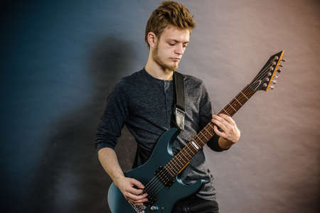 Young bearded man with electric guitar. Adult person is holding instrument and playing. Hobby, music concept, on greyの写真素材