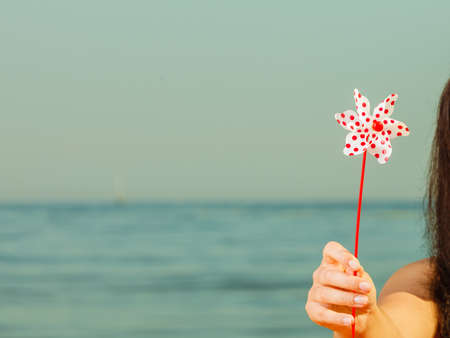 Woman hand holding little windmill, blue sea water and horizon in background.の写真素材