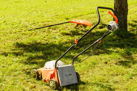 Gardening, garden service. Old lawn mower cutting green grass in backyard. Mowing field with lawnmower in sunny day.の写真素材