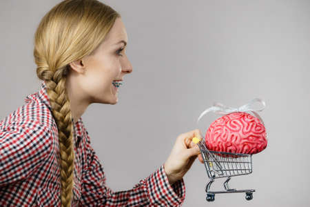 Happy woman holding shopping cart with brain inside. Clever, responsible buying concept.の写真素材