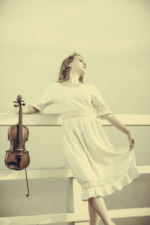Music love, hobby and everyday passion concept. Woman on pier outside holding violin during sunsetの写真素材