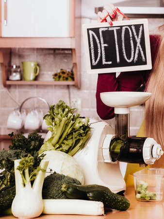 Drinks good for health, diet breakfast concept. Young woman in kitchen next to juicer machine and detox sign.の写真素材