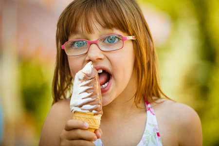 Summertime joy, summer recreation outside concept. Toddler girl in eyeglasses eating ice cream, having funの写真素材