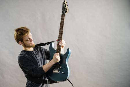 Young bearded man with electric guitar. Adult person is holding instrument and playing. Hobby, music...