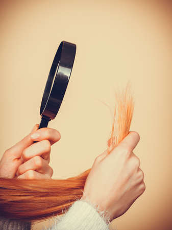 Haircare, health problem concept. Unhappy blonde woman looking at ends of her blonde hair through magnifying glassの写真素材