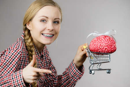 Happy woman holding shopping cart with brain inside. Clever, responsible buying concept.の写真素材