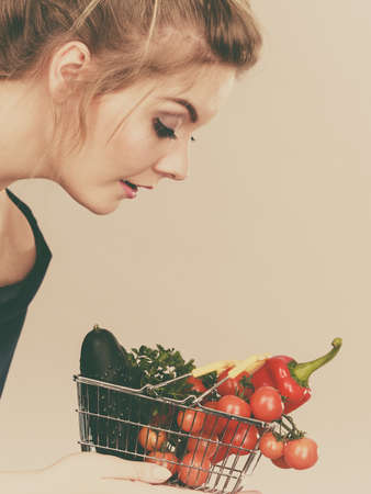 Buying good food, vegetarian products. Positive woman holding shopping basket with green red vegetables inside, recommending healthy high fibre diet, lifestyle modification, on greyの写真素材