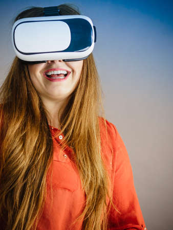 Smiling positive woman wearing virtual reality goggles headset, vr box. Connection, technology, new generation and progress concept. Studio shot on grayの写真素材