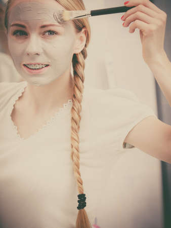 Facial dry skin and body care, complexion treatment at home concept. Happy young woman applying grey mud mask on her face with brush.の写真素材