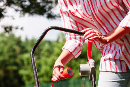 Gardening. Female person being mowing green lawn with lawnmower, in sunny day.の写真素材