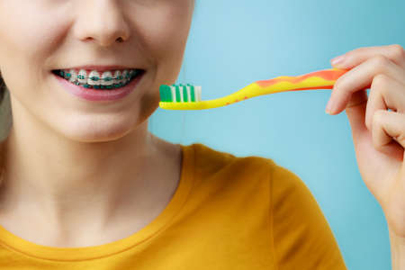 Dentist and orthodontist concept. Young woman with blue braces cleaning and brushing teeth using...