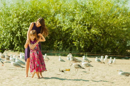 Woman and girl walking on the beach next to the boat, seagulls and bushesの写真素材