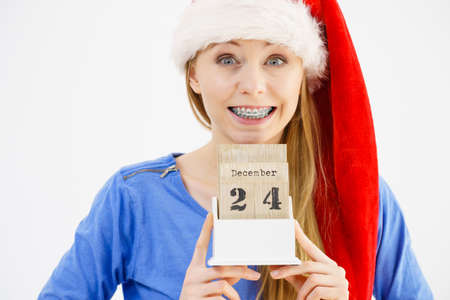 Happy positive young teenage woman wearing Santa Claus christmas hat holding calendar with 24...
