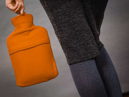 Woman holding warm orange hot water bottle. Fever, flu treatment objects concept.