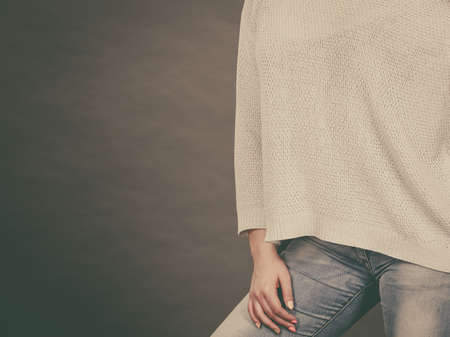 Unrecognizable woman wearing light white oversize sweater jumper and blue tight jeans. Grey...