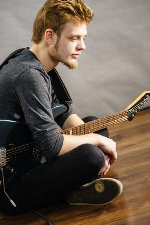 Young bearded man with electric guitar. Adult person is holding instrument and playing. Hobby, music...