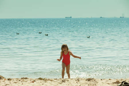 Vacations with kids concept. Little toddler girl playing on beach wearing swimsuit, having fun.の写真素材