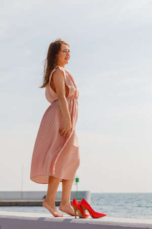Hobby, idyllic aspects of femininity concept. Woman walking on jetty without shoes wearing beautiful long light pink dress.の写真素材