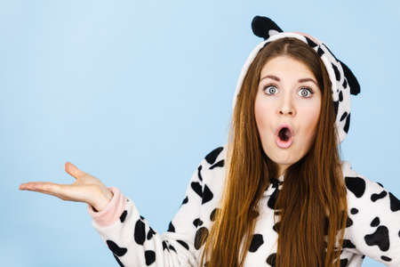 Happy teenage girl in funny nightclothes, pajamas cartoon style presenting something, holding open empty hand with positive face expression, studio shot on blue. Advertisement concept.の写真素材
