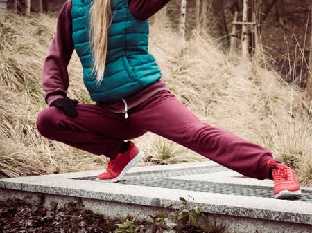 Sport and recreation. Fit slim sporty teen girl stretching warming up outdoor in park. Woman exercising on fresh air.の写真素材