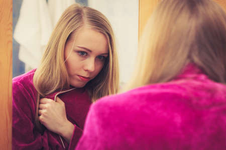 Happy awaken woman standing in bathroom looking at her reflection in mirror after morning getting upの写真素材