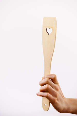 Woman hand holding wooden kitchen spatula with heart love symbol. Cooking utensils concept.の写真素材