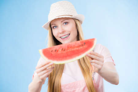Happy cheerful teenage young woman ready for summer wearing pink outfit and sun hat holding sweet fruit red juicy watermelonの写真素材