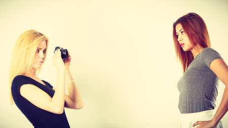 Photographer and model. Blonde girl shooting images, taking photos with camera, photographing mulatto female modelの写真素材