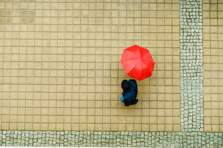 Person walking on city street during rainy day holding umbrella protecting from rain. High angle top...