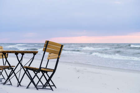Beautiful relaxation place on sandy beach. Wooden chairs and table during sunsetの写真素材