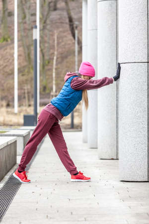 Sport and recreation. Fit slim sporty teen girl stretching warming up outdoor on city street. Woman...