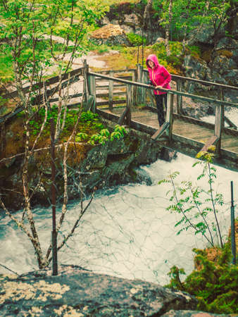Travel and hiking. Tourist woman standing on bridge, enjoying waterfall torrential river along the Aurlandsfjellet mountains in Norway Sogn og Fjordane, foggy hazy summer dayの写真素材