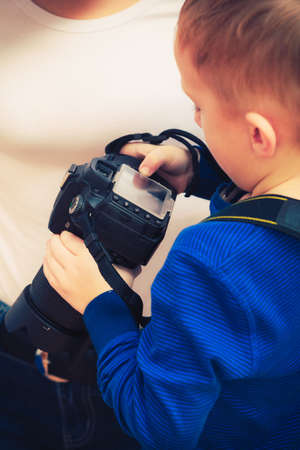Child passion and hobbies concept. Kid playing with big professional digital camera, photographing various things in houseの写真素材
