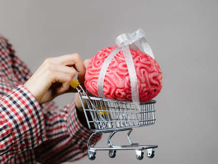 Happy woman holding shopping cart with brain inside. Clever, responsible buying concept.の写真素材