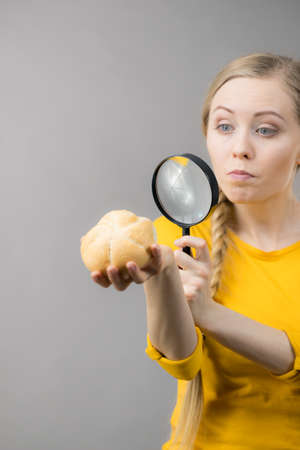 Woman holding bun bread roll and magnifying glass examine wheat product ingredients
