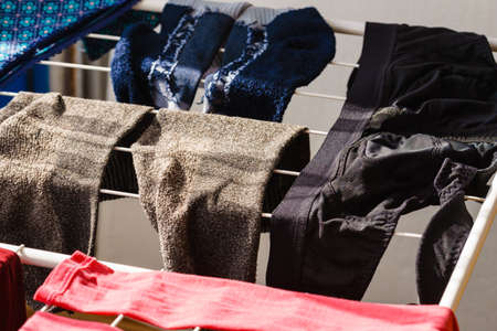 Many colorful clothes from laundry hanging on drying rack at home next to window.の写真素材