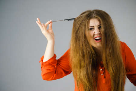 Funny teenage woman having problem with tangled tousled hair. Haircare problems concept.の写真素材